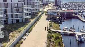 A marina with boats, a walkway, and modern buildings with balconies. - 5 Star Holiday Home in Wendtorf (Wendtorf)