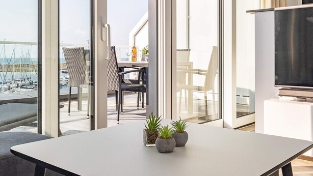A modern room with a large window, a flat-screen TV, and a dining table with potted plants. - 5 Star Holiday Home in Wendtorf (Wendtorf)