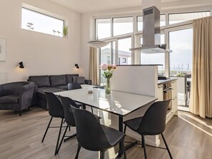 Um espaço de estar moderno com área de jantar, sofá, cozinha e grandes janelas.