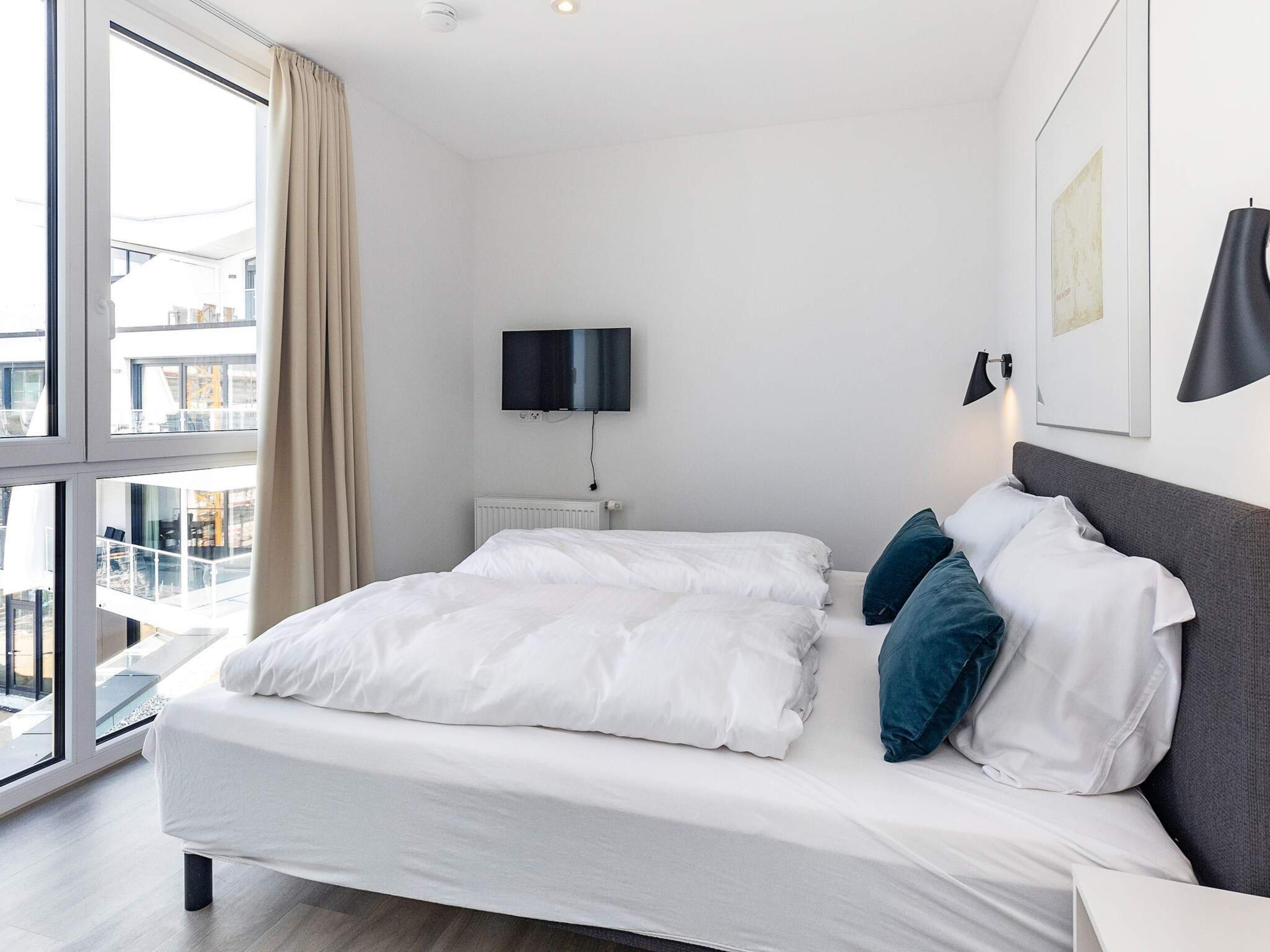 Ett modernt hotellrum med en stor säng, en platt-TV som är monterad på väggen och utsikt över staden genom stora fönster.