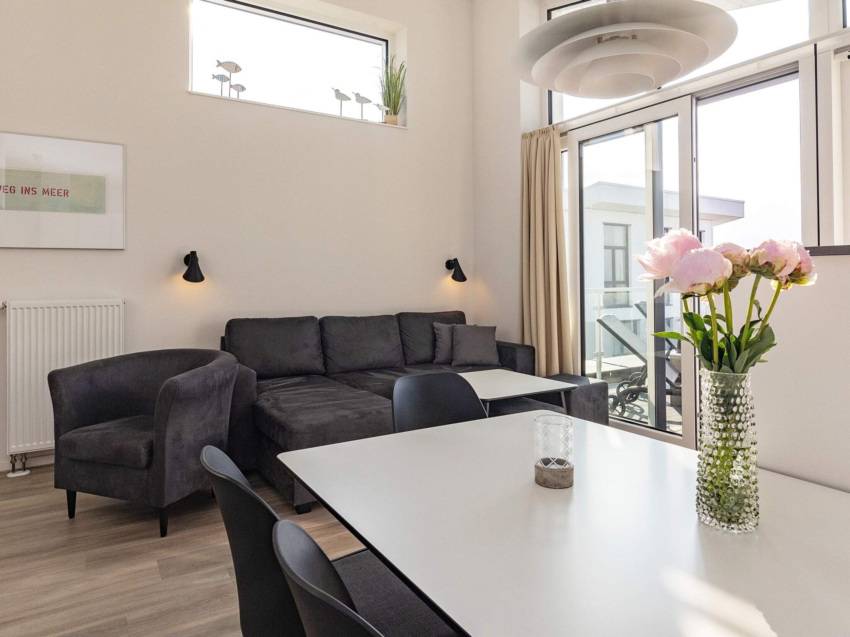 A modern living room with a sectional sofa, a dining table, and a vase with flowers.