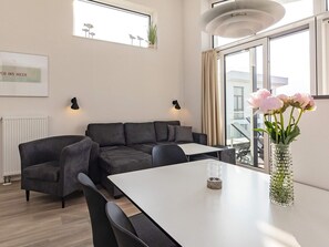 A modern living room with a sectional sofa, a dining table, and a vase with flowers.