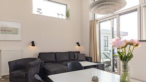 A modern living room with a sectional sofa, a dining table, and a vase of flowers. - 5 Star Holiday Home in Wendtorf (Wendtorf)
