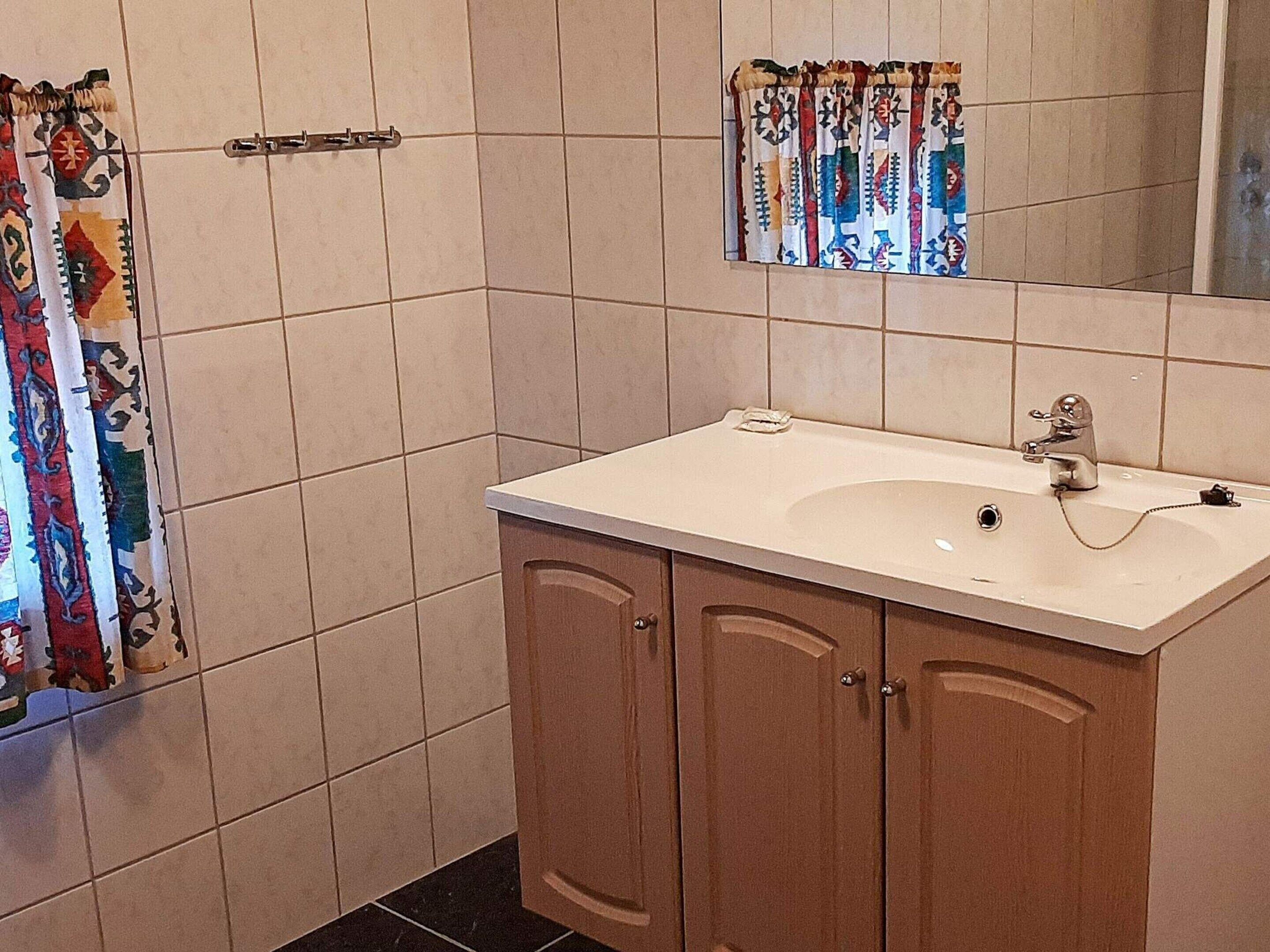 A bathroom with a white sink, wooden cabinets, a towel rack, and a shower curtain.