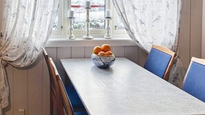 A dining area with a wooden table and blue chairs, a bowl of oranges on the table, and a window with curtains. - 4 Person Holiday Home in Skulestadmo (Voss)