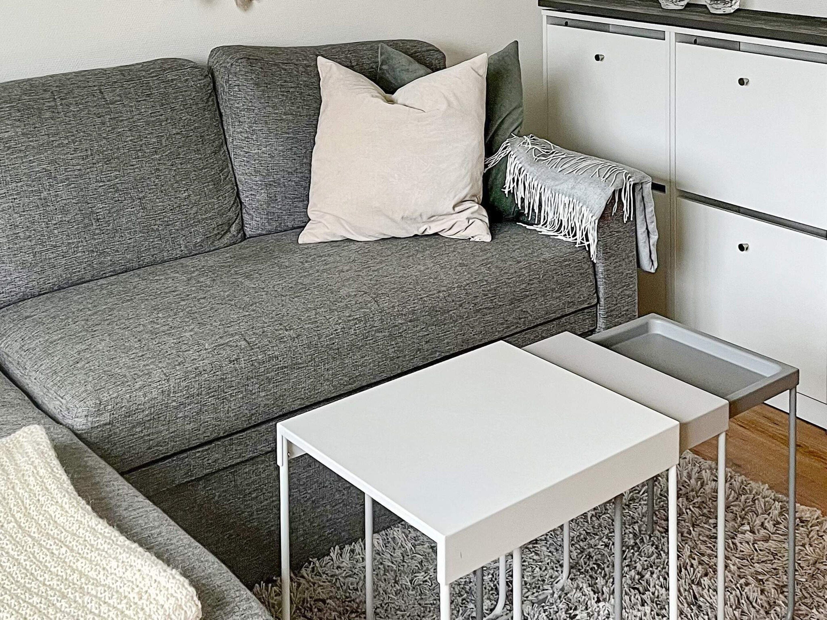 A grey sofa with a white pillow and a white side table in a room with a white cabinet and a grey shag rug.