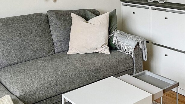 A grey sofa with a white pillow and a white side table in a room with a white cabinet and a grey shag rug. - 5 Person Holiday Home in Salen (Salen)