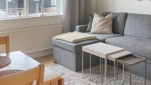 Un salon moderne avec un canapé gris, une petite table et une fenêtre avec des rideaux.