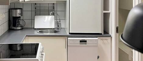 Eine kompakte Küche mit Kaffeemaschine, Spüle, Kühlschrank und Geschirrspüler.
