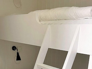 A white bed with a pillow, a white bedside table, and a wall-mounted light fixture. - 5 Person Holiday Home in Salen (Salen)