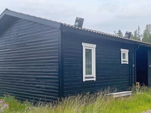 A small, dark-colored wooden cabin with a single window and a chimney.
