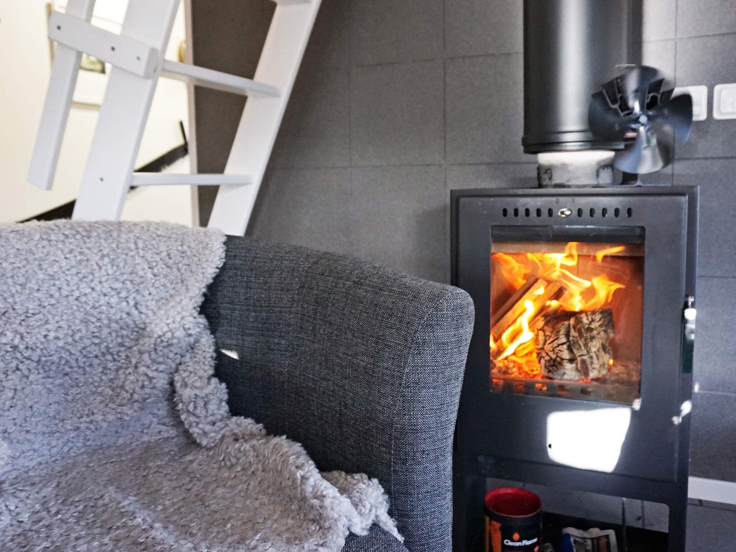 A room with a grey sofa, a white chair, and a wood-burning stove.