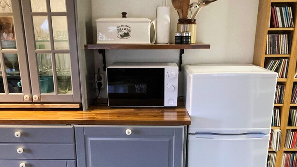 Una cocina con microondas, un refrigerador blanco y un estante de madera con utensilios de cocina.
