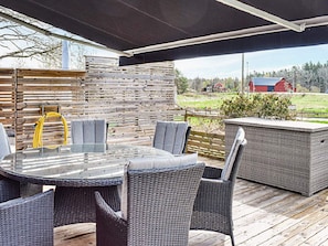 An outdoor patio with a round table and wicker chairs, a covered area, and a view of a rural landscape. - 4 Star Holiday Home in Paryd (Påryd)