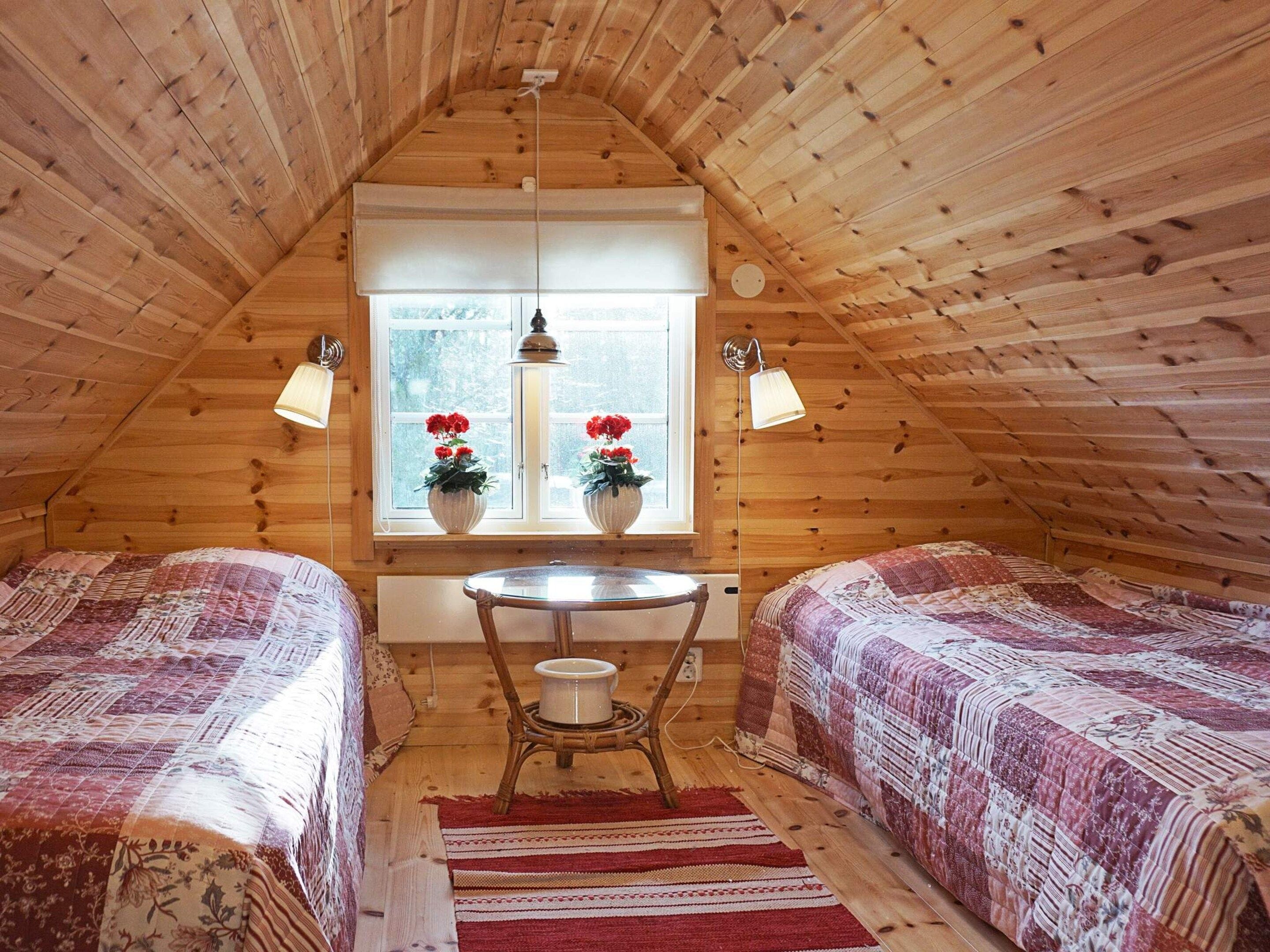 A cozy attic bedroom with two beds, a small table, and a window with potted plants.