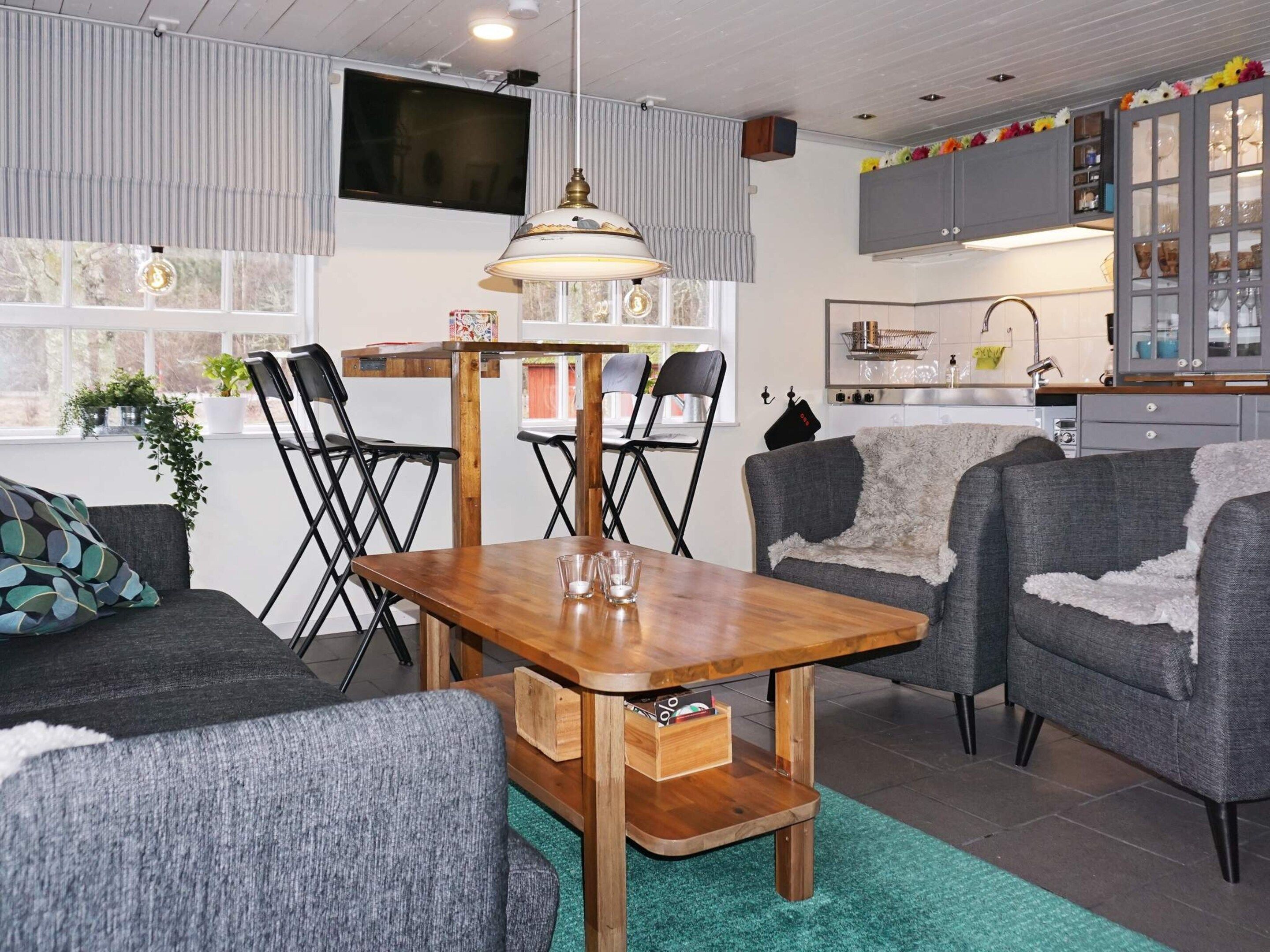 A modern living room with a wooden dining table, grey sofas, and a kitchen in the background.