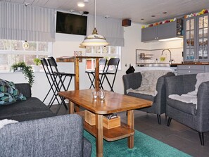 A modern living room with a wooden dining table, grey sofas, and a kitchen in the background. - 4 Star Holiday Home in Paryd (Påryd)