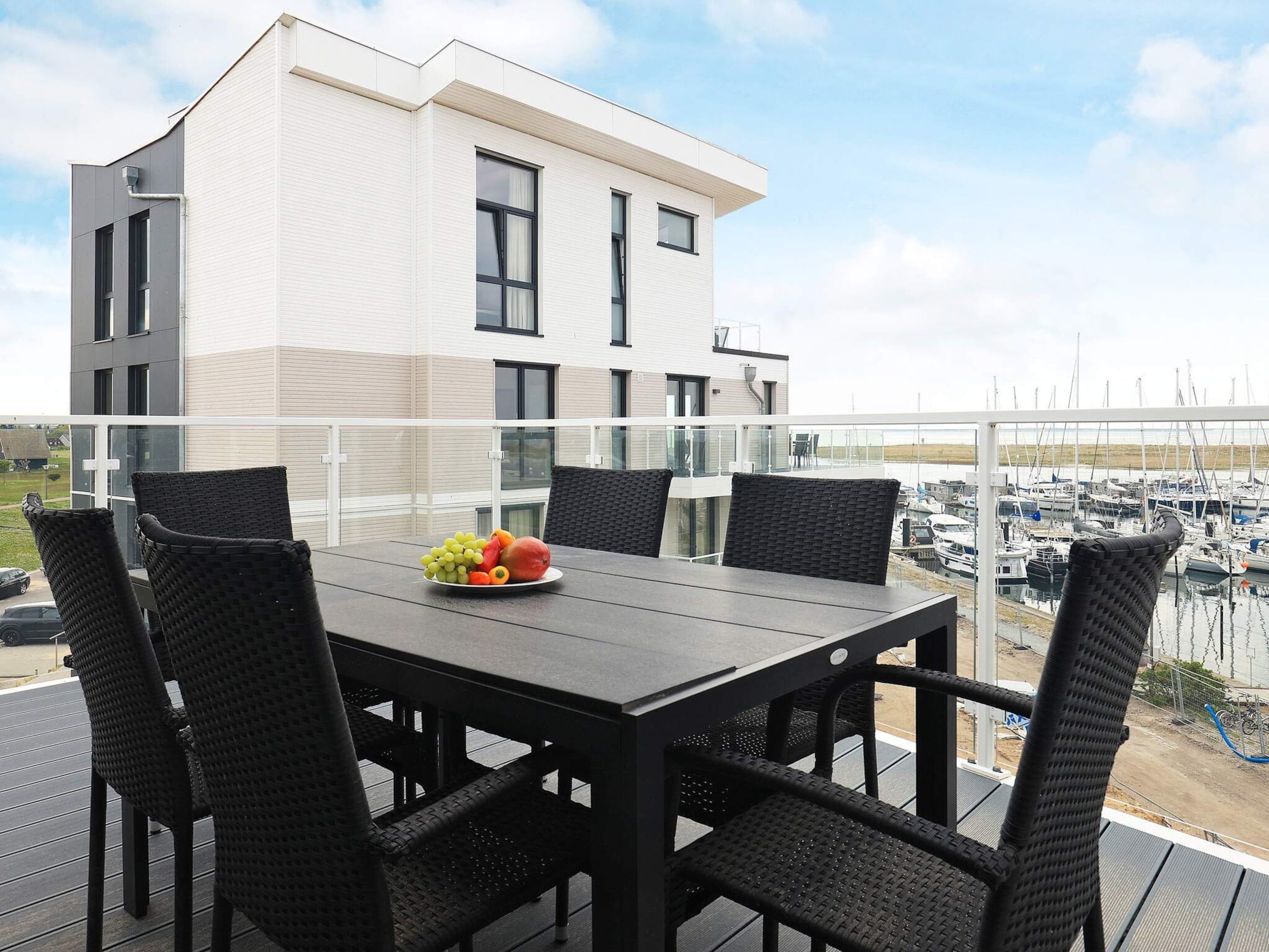 Un balcon avec une table et des chaises, un panier de fruits et une vue sur une marina remplie de bateaux.