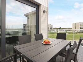 A balcony with a table and chairs, a plate of fruit, and a view of the sea and buildings.