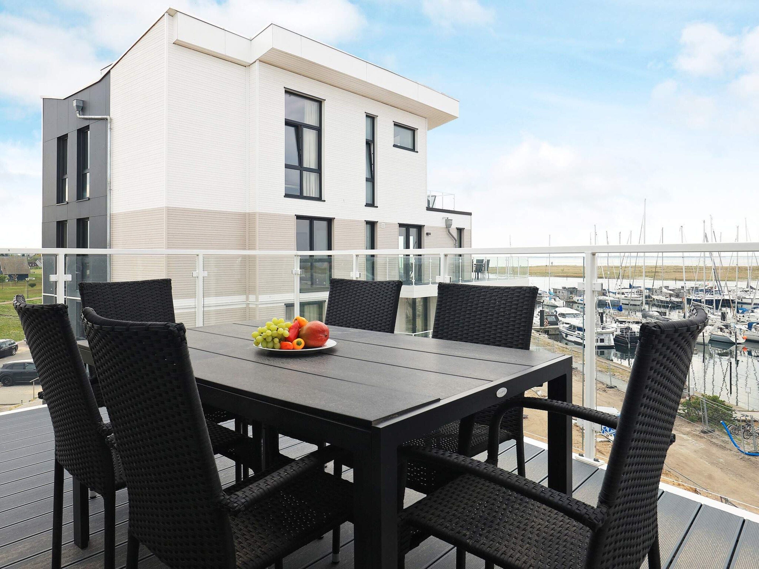 A balcony with a table and four chairs, overlooking a marina with boats.