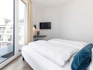 A hotel room with a bed, a TV mounted on the wall, a window with curtains, and a view of the outside. - 5 Star Holiday Home in Wendtorf (Wendtorf)