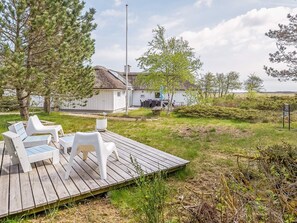 A wooden deck with outdoor furniture, a thatched-roof building, and a view of the landscape.