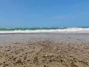 Une plage avec des vagues, des galets et un ciel dégagé.
