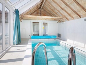 Une piscine dotée d’une structure en verre, d’un plafond en bois et offrant une vue sur l’extérieur.