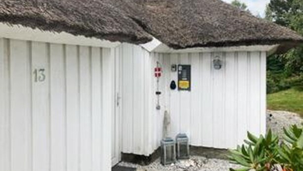 A white building with a thatched roof, a door with a red and white sign, and two small lanterns outside. - 4 Star Holiday Home in Fjerritslev (Fjerritslev)