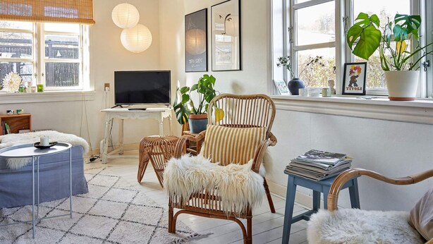 Una sala de estar acogedora con televisor, sillas de mimbre, una mesita y una ventana con plantas.