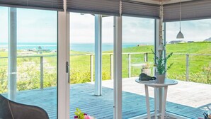 A room with a large sliding glass door leading to a balcony with a view of the sea and green landscape. - 6 Person Holiday Home in Lemvig (Lemvig)