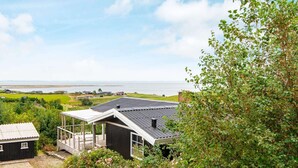 A coastal property with a large house featuring a covered porch, a smaller adjacent building, and a view of the sea and distant landscape. - 6 Person Holiday Home in Lemvig (Lemvig)