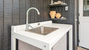 A small outdoor kitchen with a sink, a faucet, and a shelf with pots and a bottle. - 6 Person Holiday Home in Lemvig (Lemvig)