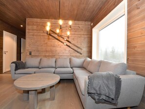 Un intérieur moderne avec un plafond en bois, un grand canapé, une table ronde et une grande fenêtre.