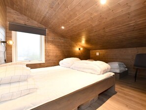 Une pièce aux murs lambrissés, avec un lit, une chaise et une fenêtre.