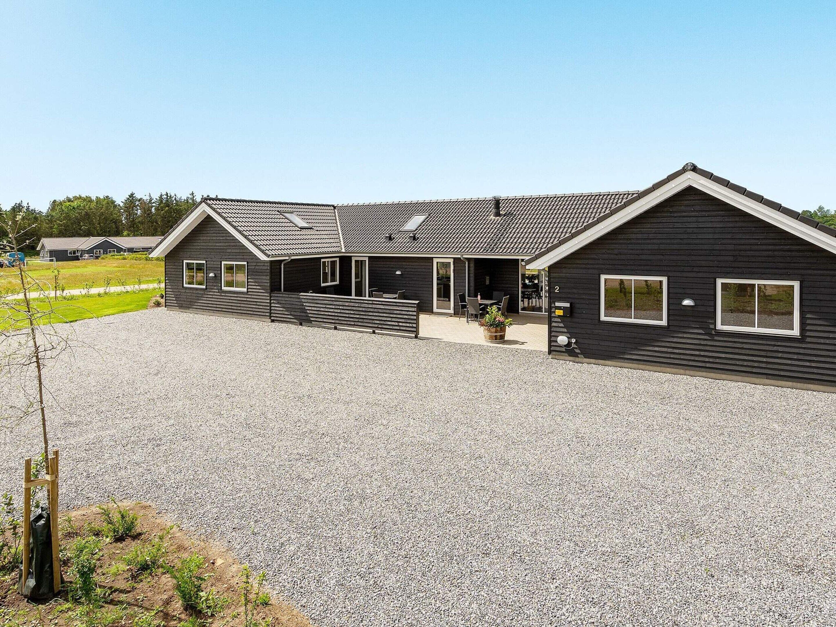 A modern two-story house with a gravel driveway and a covered patio area.