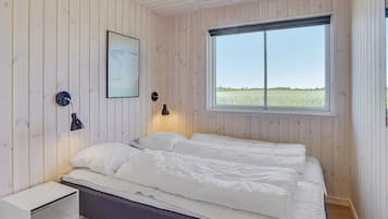 Un dormitorio con cama, lámparas de noche, una ventana con vistas a un campo y una mesita de noche blanca.