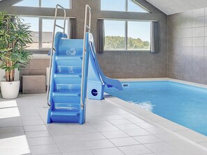 Una piscina interior con un tobogán azul y una planta en maceta.