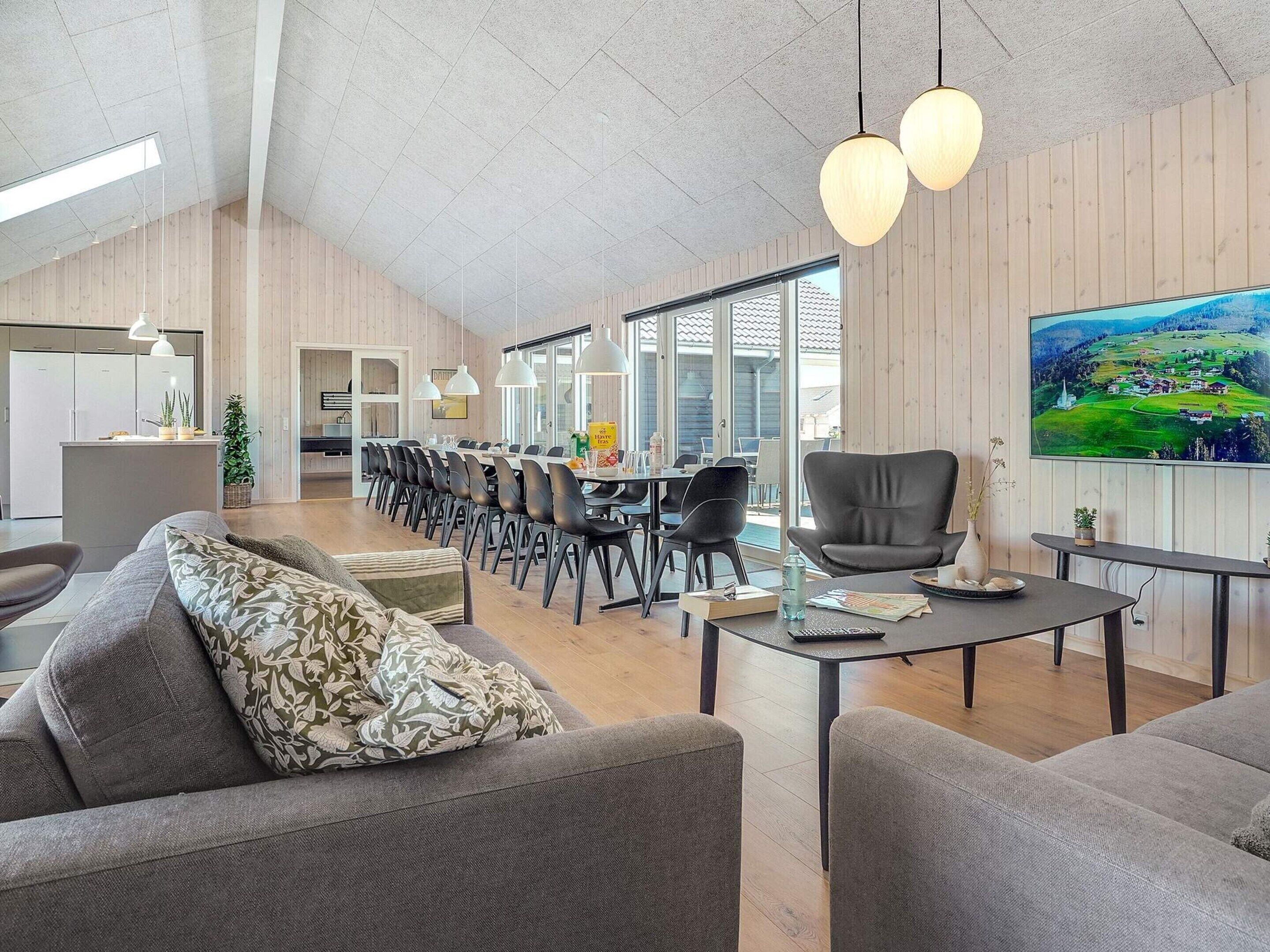 A spacious living area with a dining table and chairs, a sofa with patterned cushions, and a painting of a landscape on the wall.