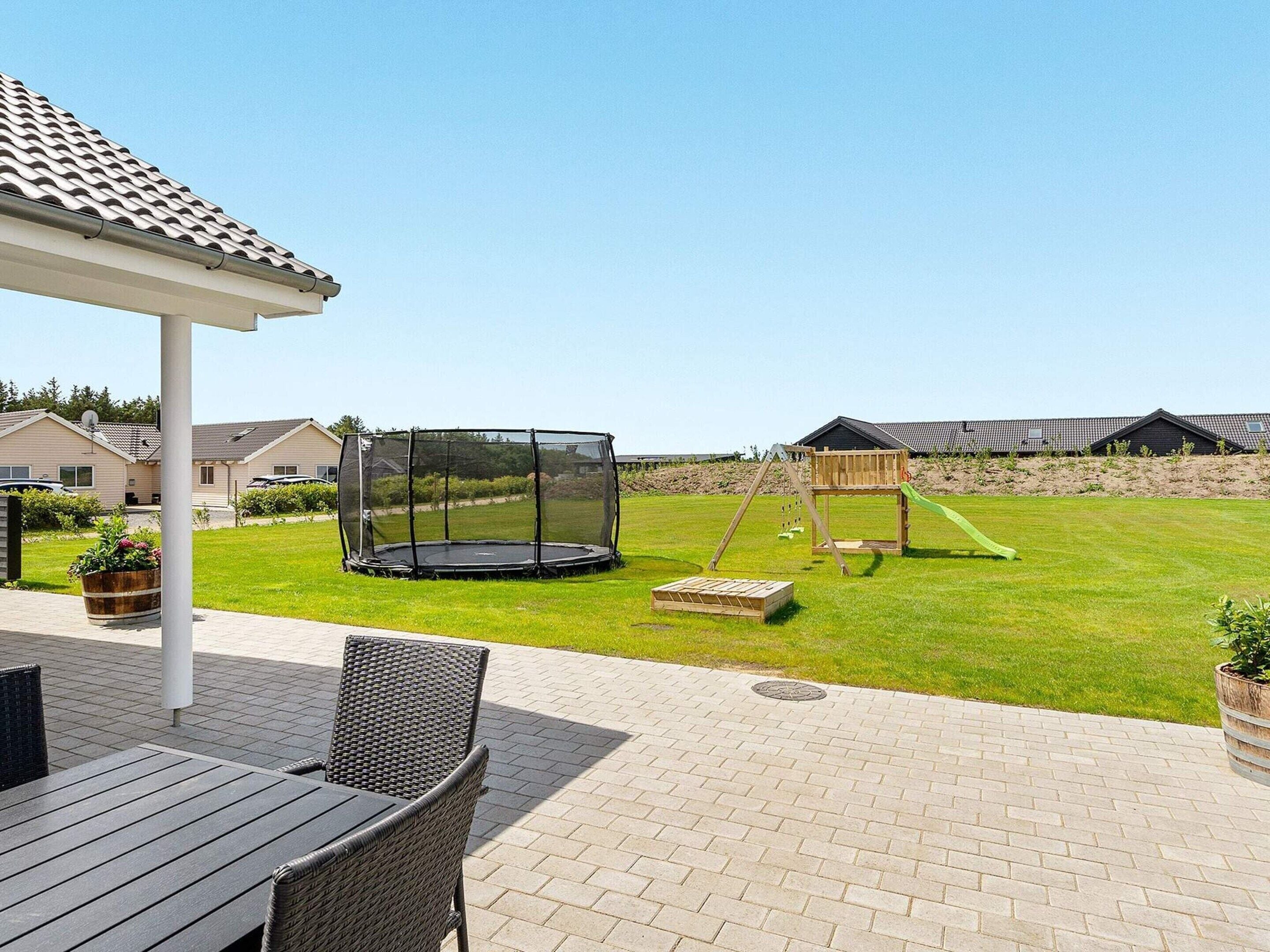A patio area with a table and chairs, a trampoline with a safety net, and a wooden play structure.
