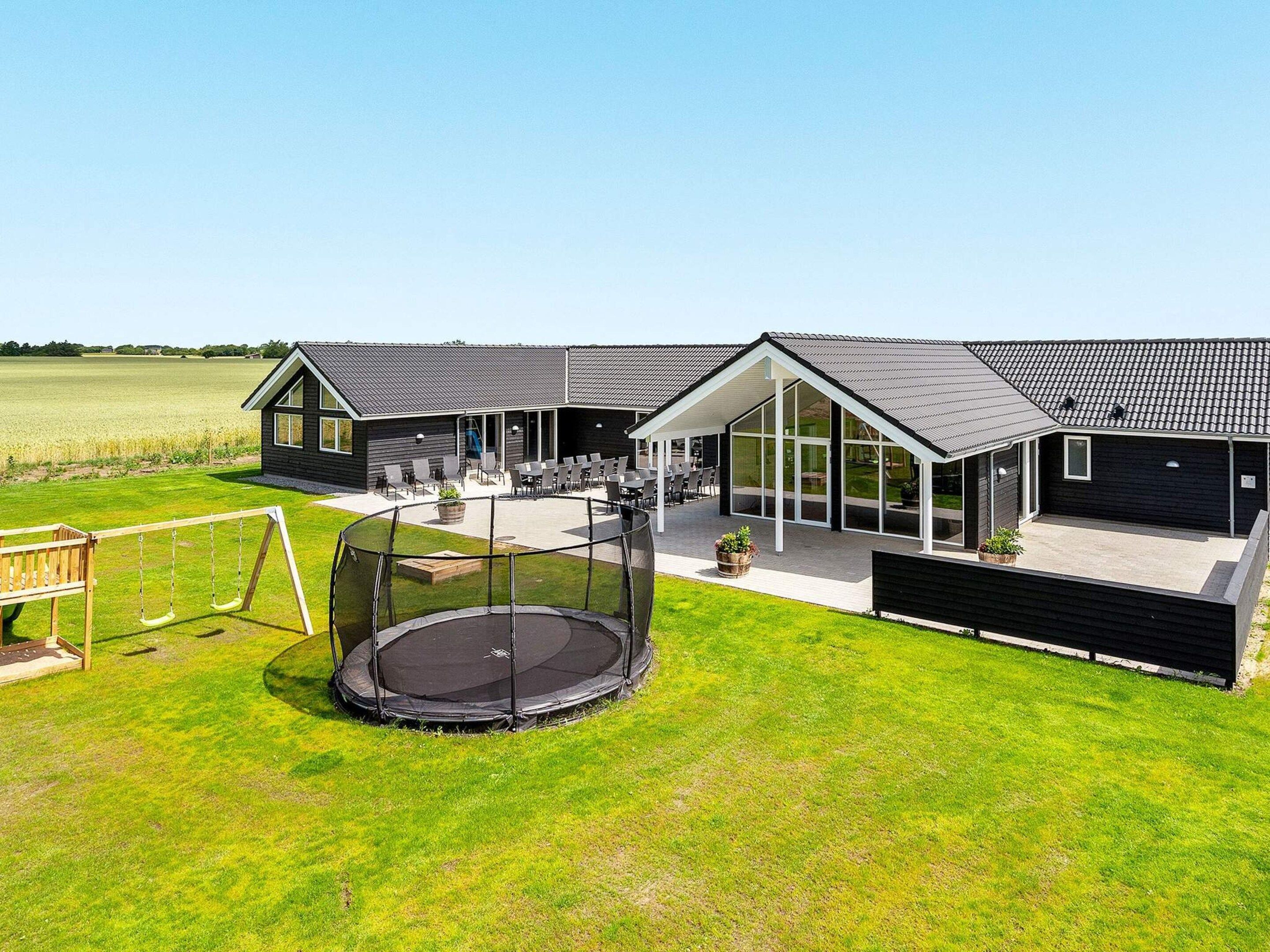 A modern house with a large patio, a trampoline, and a swing set.