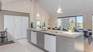 Una cocina moderna con una isla central, electrodomésticos integrados, iluminación colgante y vistas a un comedor.