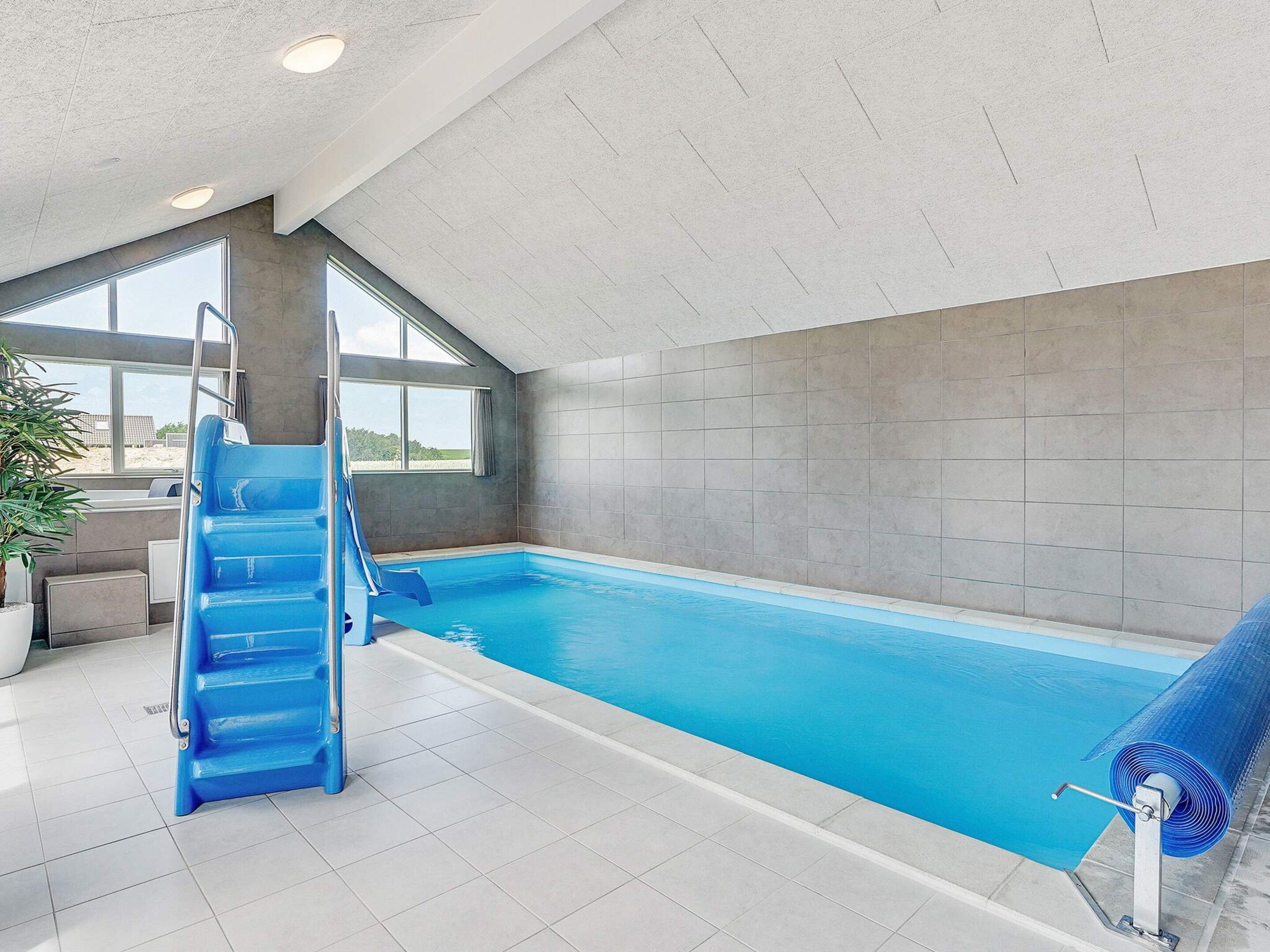 An indoor swimming pool with a blue slide, large windows, and a view of the outdoors.