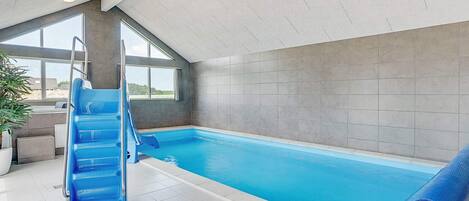 An indoor swimming pool with a blue slide, large windows, and a view of the outdoors.