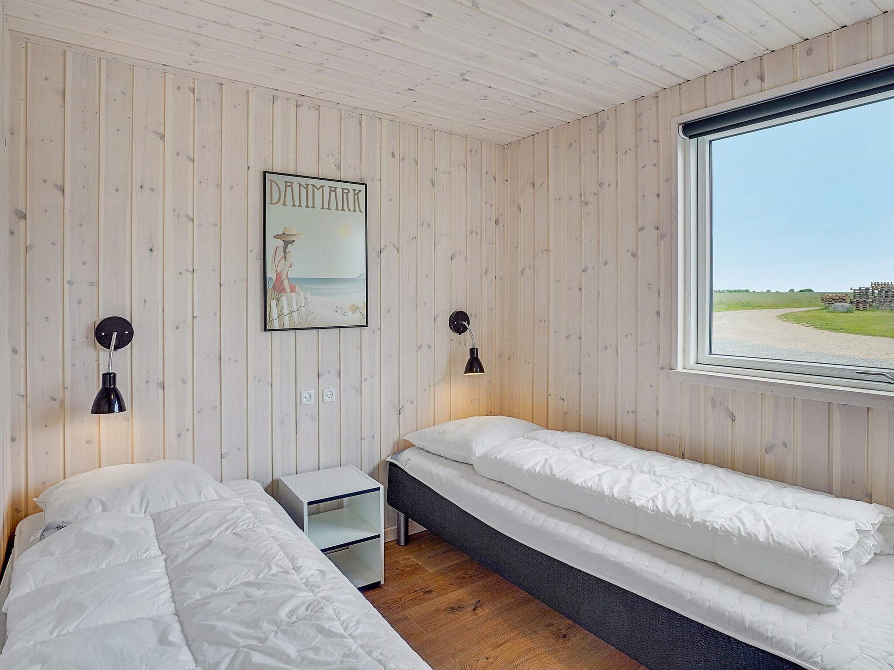 Quarto com duas camas, janela com vista para a praia, pintura de um farol e luminária na parede.