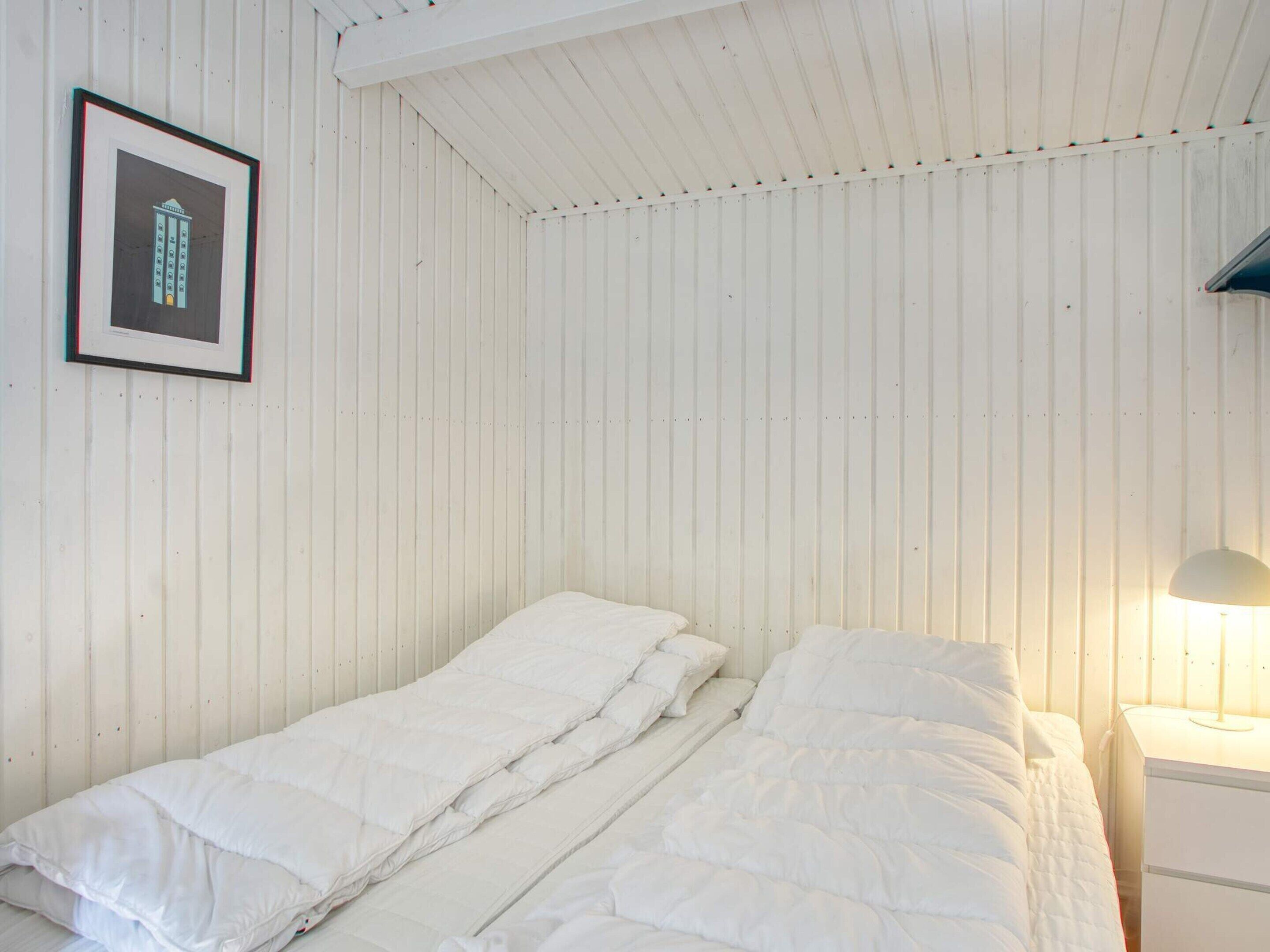 A room with a bed, a nightstand, a framed picture, and a lamp.