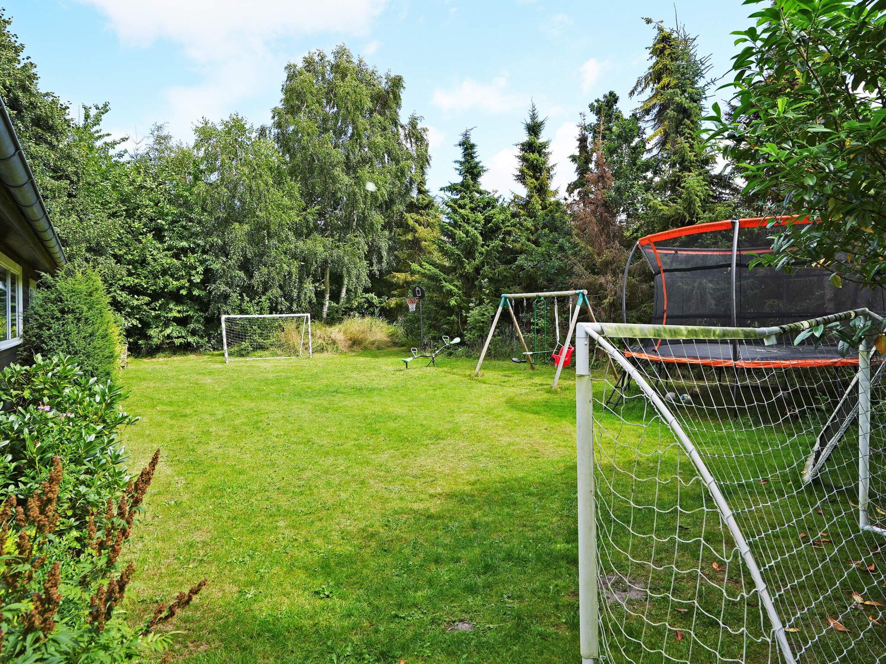 Een omheinde achtertuin met een trampoline, een voetbalkooi en een schommel.