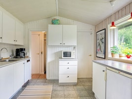 Una cocina compacta con armarios blancos, microondas, cafetera y ventana con vistas al verdor.