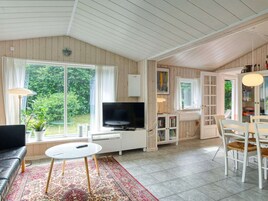 Una habitación con televisión, una mesa de comedor, sillas, una estantería y una ventana con cortinas.