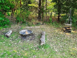 An outdoor fire pit surrounded by natural foliage and a metal grill structure.